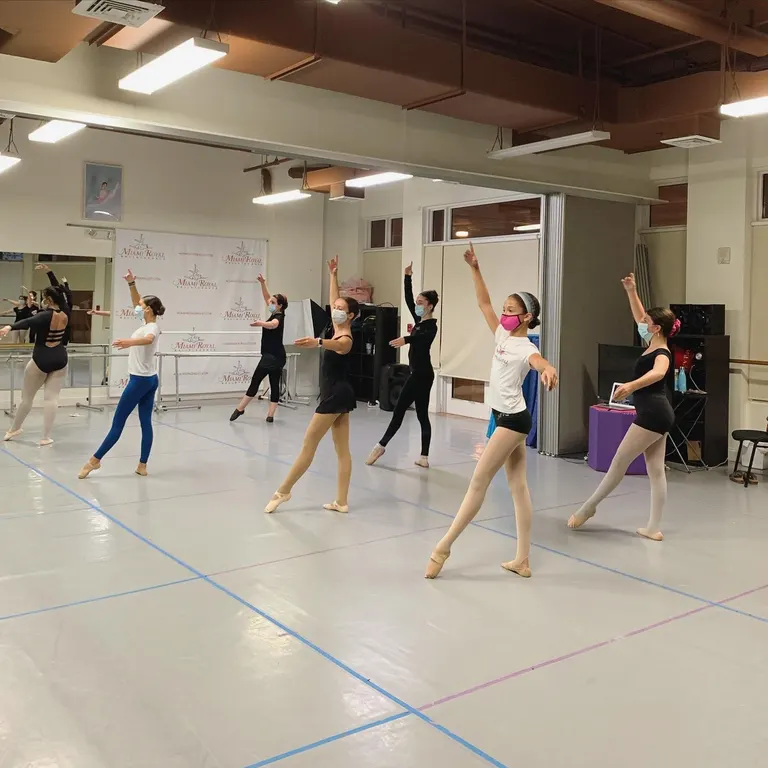 Adult dancers practicing a ballet combination together in a mirrored studio